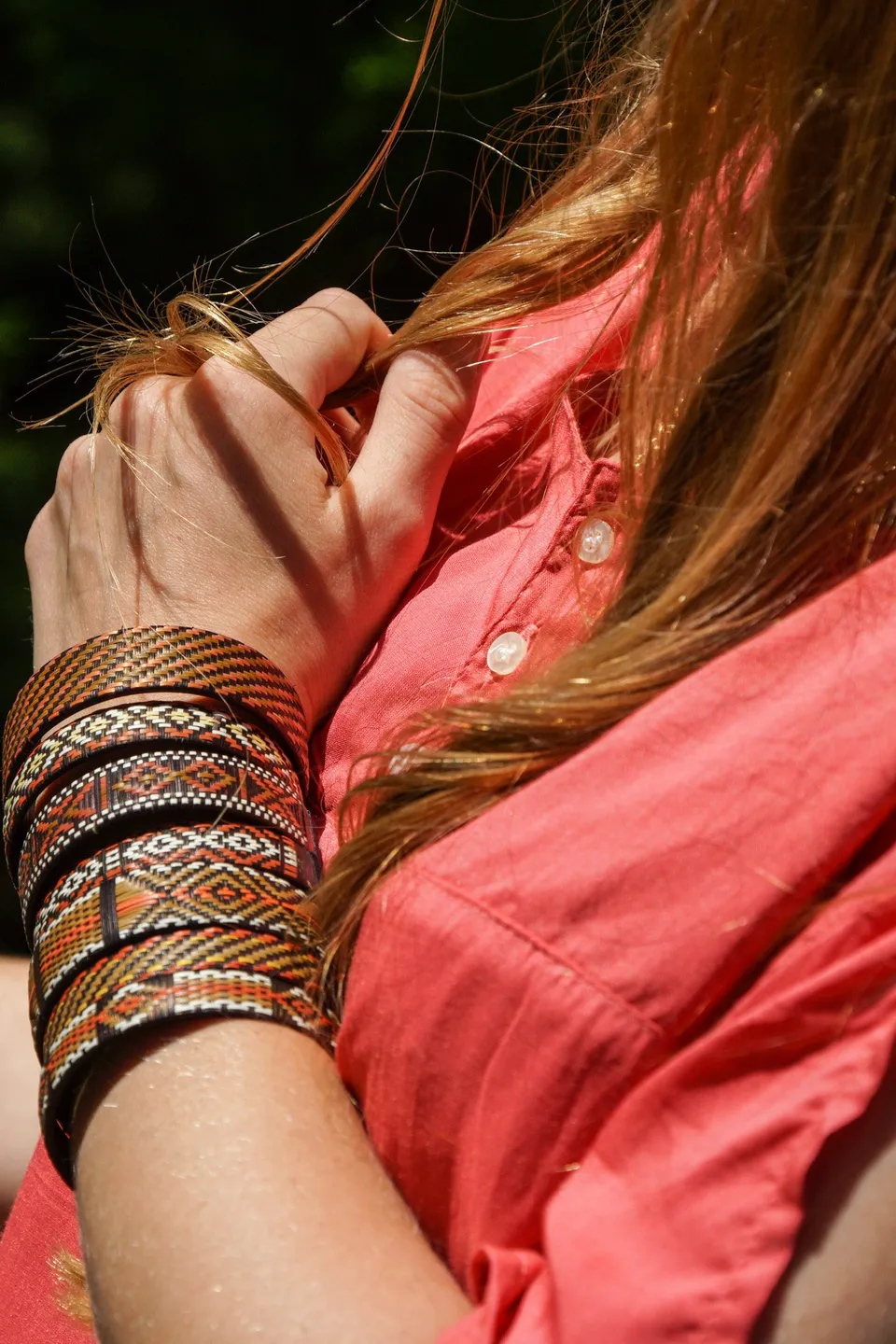 Mains au col d'une chemise corail, poignet chargé de bracelets tissés et d'un jonc doré, à Porquerolles.