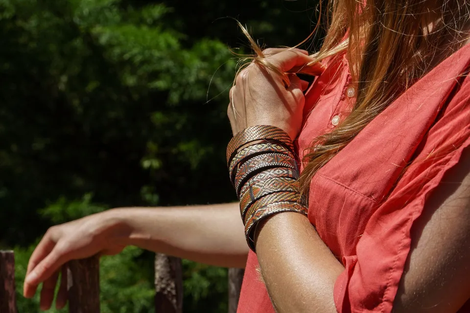 Bras posé sur une barrière de bois, bracelets tissés au poignet, feuillage vert derrière, à Porquerolles.
