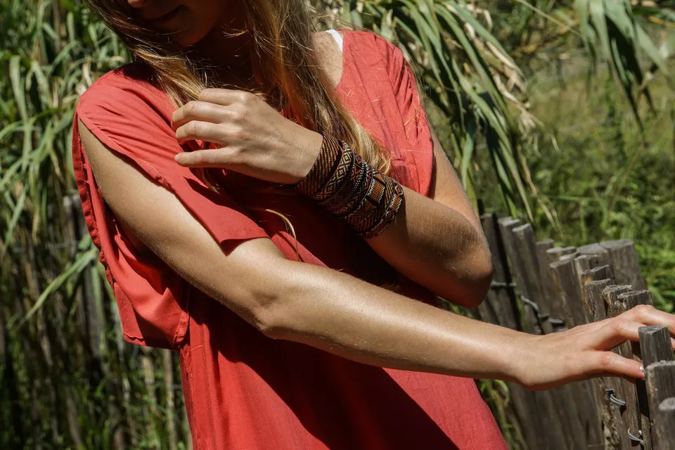 Femme en tunique terracotta et bracelet tissé appuyée à une clôture de bois parmi les roseaux à Porquerolles.